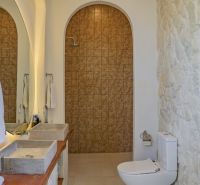 A bathroom in a villa with a stone wall, double sink, and a shower behind an arch.