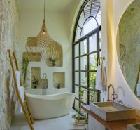 A bathroom in a villa with a bathtub, stone walls, and a large arched window.