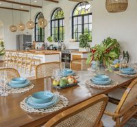 The dining room of the villa with a table, cutlery, blue plates, and plants, floor with wooden decor.