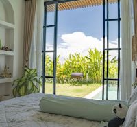 Bedroom in a villa with a view of the garden and pool, decorated with plants.
