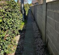 A narrow path by the wall between flowers and a fence on Hrušovská in Bratislava, Vrakuňa district, plots - residential area.