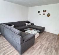 Living room with a corner sofa, glass table, and floor with wood decor.
