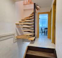 Interior of a two-story apartment with wooden stairs and an entrance to a room.