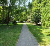 A sidewalk surrounded by greenery on J. Emanuela Street in the town of Vrbové, next to a 2-room apartment.