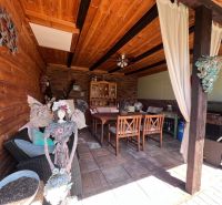 Covered seating area with wooden paneling in a family house, decorated with a statue and curtains.