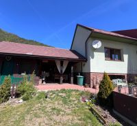 A family house in Švošov with a terrace and a garden, surrounded by mountains and a blue sky.