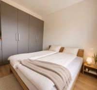 A bedroom in a two-room apartment with a wooden decor floor, a large wardrobe, and a nightstand.