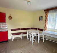 A kitchen in a family house with yellow walls, a red kitchen unit, and a bench.