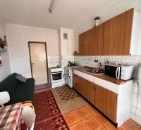 A kitchen in a family house with older furnishings, tiles, and wooden cabinets.