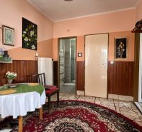 A room in a family house decorated with paintings, a table with a tablecloth, and a carpet.