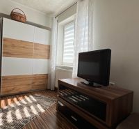 A room in a 3-room apartment with a dresser, a television, and a floor with a wood decor.