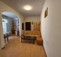A room in a 3-room apartment with a wood-decor floor, a sofa, and a kitchenette.