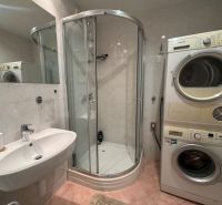 A bathroom with a washing machine, dryer, and shower in a 3-room apartment.