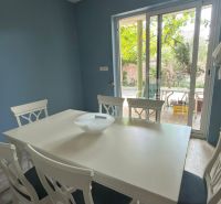 Dining area with a white table and chairs, wooden decor flooring, garden view.