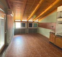 A room with a wooden ceiling, a floor with a wooden decor, and kitchen cabinets.