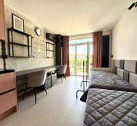 Studio apartment with beds, work desks, modern decor, and a balcony view.