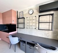 A studio apartment with a wooden decor floor, a pink kitchen, and gray work chairs.