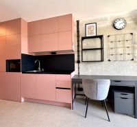 A kitchen and a work corner in a studio apartment with modern shelves and a clock on the wall.
