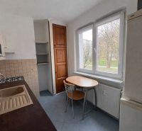 A kitchen in a 2-room apartment with wooden cabinets and a table by the window.
