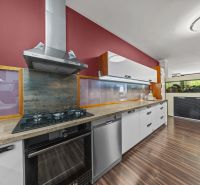 A family house kitchen with a red wall, modern appliances, and a wooden decor floor.