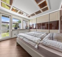 Bedroom with wood-decor flooring, a wardrobe, and a large window in a family house.