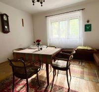 A dining room in a family house with simple furniture, a clock, and a cross on the wall.