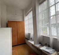 A hallway with large windows, wooden floor decor, a cabinet, and a white refrigerator.