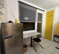 A kitchen in a studio apartment with a fridge, a table, and yellow cabinets.