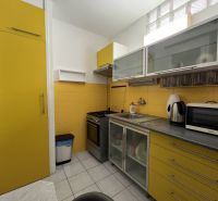 A kitchen in a studio apartment with bright yellow cabinets and white tiles.