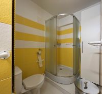 Bathroom with toilet and shower in a studio apartment, yellow tiles.