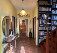 The hallway of a family house with a library, staircase, mirror, and shelf.
