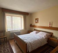 Bedroom in a family house with a bed, chair, carpet, and wooden decor flooring.