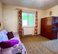 A family house: a room with a carpet, a sofa, a window, and a cabinet, leading to a bedroom.