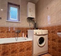 A bathroom in a family house with a bathtub, washing machine, and gas boiler.