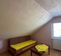 Attic room in a family house with a window and a bed, floor with wooden decor.