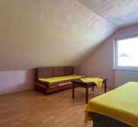 A bright attic room with two beds, a table, and a wooden decor floor.