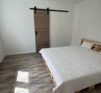 A bedroom in a family house with a pallet bed, sliding doors, and a floor with a wooden decor.