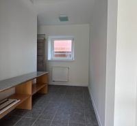 A narrow space with a window, radiator, shelves, and gray floor in a family house.
