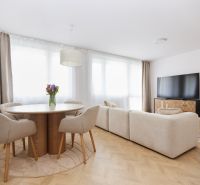 Living room with wood-patterned flooring in a 4-room apartment, seating area and table with flowers.