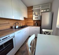 A kitchen with white cabinets and appliances, equipped with wood-patterned flooring in a 2-room apartment.