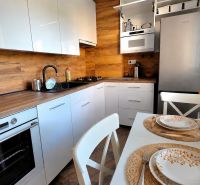 A kitchen in a 2-room apartment with white cabinets, a wood-patterned floor, and a table with flowers.