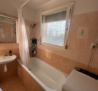 Bathroom in a 3-room apartment with a bathtub, sink, and washing machine, tiles with warm tones.