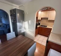 A kitchen with wooden decor, a dining table, a refrigerator, and an arch leading to the living room.