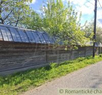 A wooden fence by a family house in Šumiac, surrounded by trees and a road.