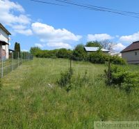Plots - housing in Karna, grassy area with fencing and adjacent buildings.