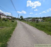A path surrounded by grass leads through a rural area in Karna with a view of houses.
