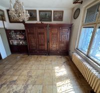 A room in a family house with furniture, paintings, a chandelier, and a radiator.