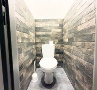 Toilet in a family house with brick wall cladding and gray flooring.