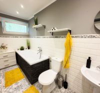 A bathroom in a family house with tiles, a bathtub, and yellow accessories.
