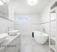 A bathroom in a family house with a bathtub, two sinks, and a shelf.